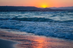 A vibrant sunset over a tropical beach with a cloudy sky.
