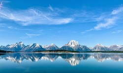 Panoramic view of Grand Teton National Park mountains and reflective lake.